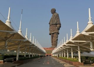 Massive statue overlooks a long pathway with white structures.