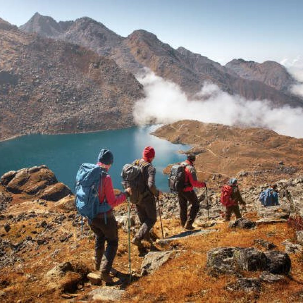 Group of tourists with backpacks descends down mountain trail to lake during a hike in the national park Lantang, Nepal.