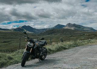 black motorcycle parked on gray asphalt road near green grass field and mountain under white clouds
