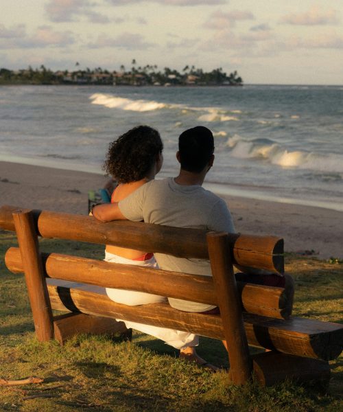 Couple embracing on a wooden bench overlooking the ocean at sunset. Perfect for romance and travel themes.